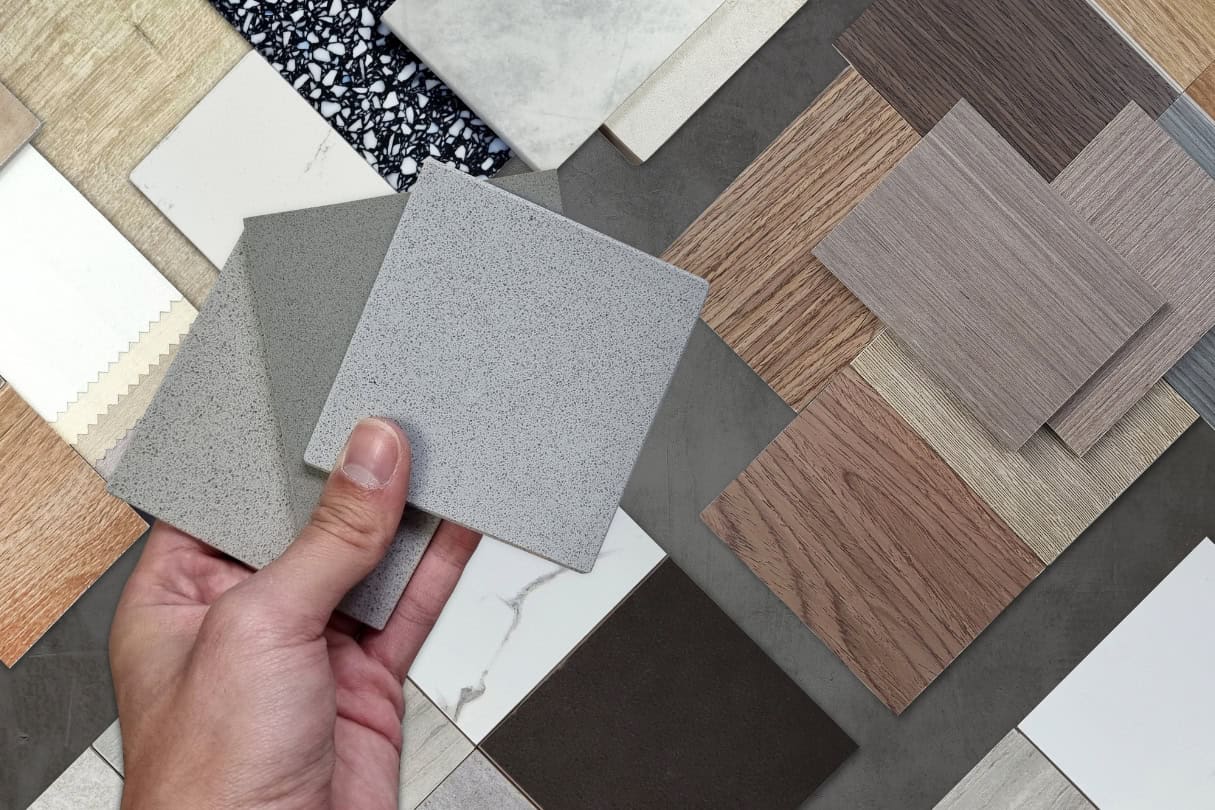 Hand holding sample tiles with various textures and colours for washroom flooring and wall design.