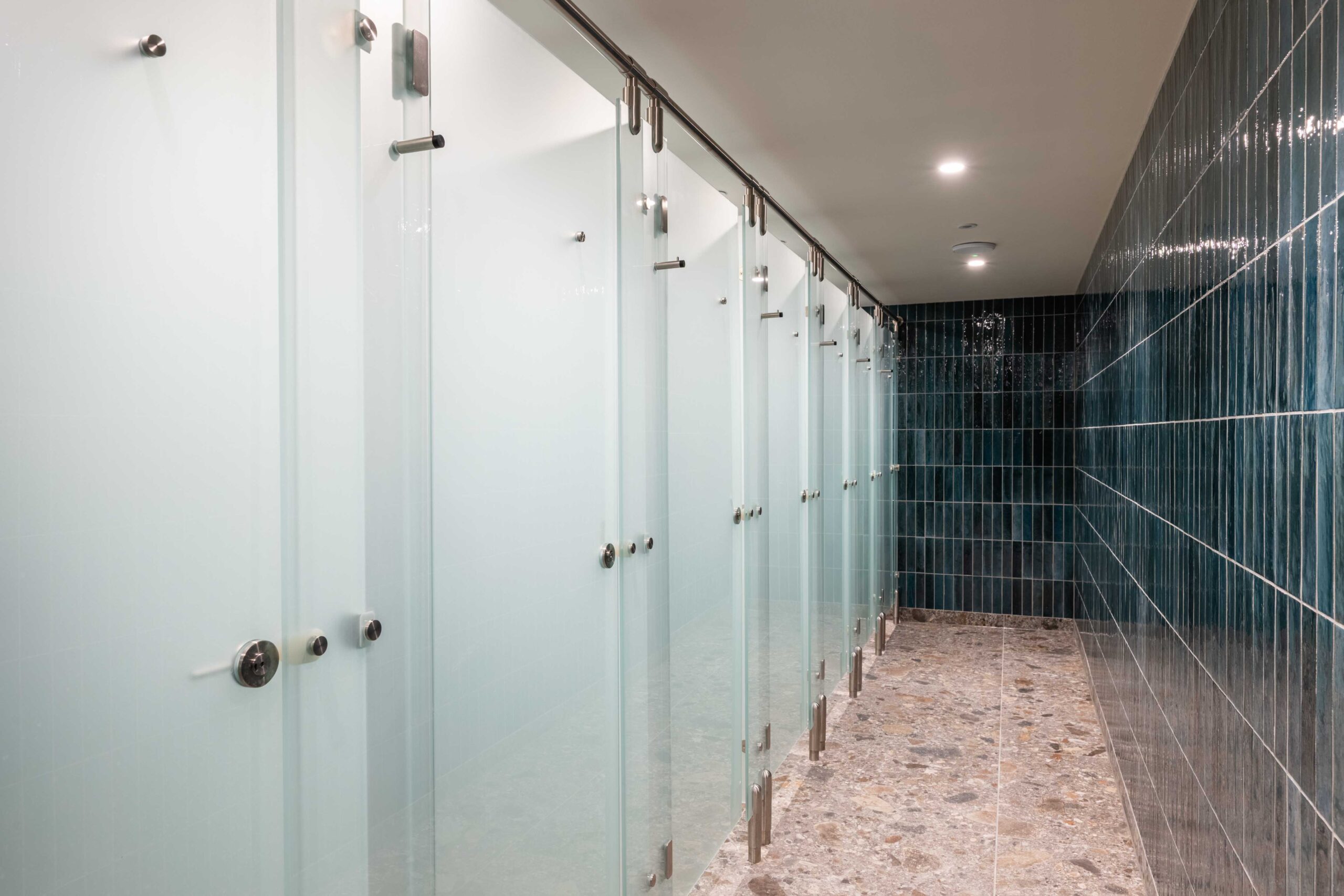 Public washroom with glass cubicles and tiled dark blue walls.