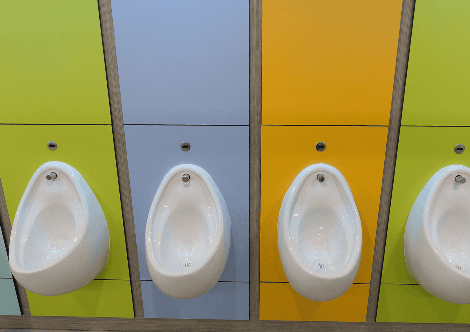 Urinals in a modern public restroom with vibrant coloured partitions.