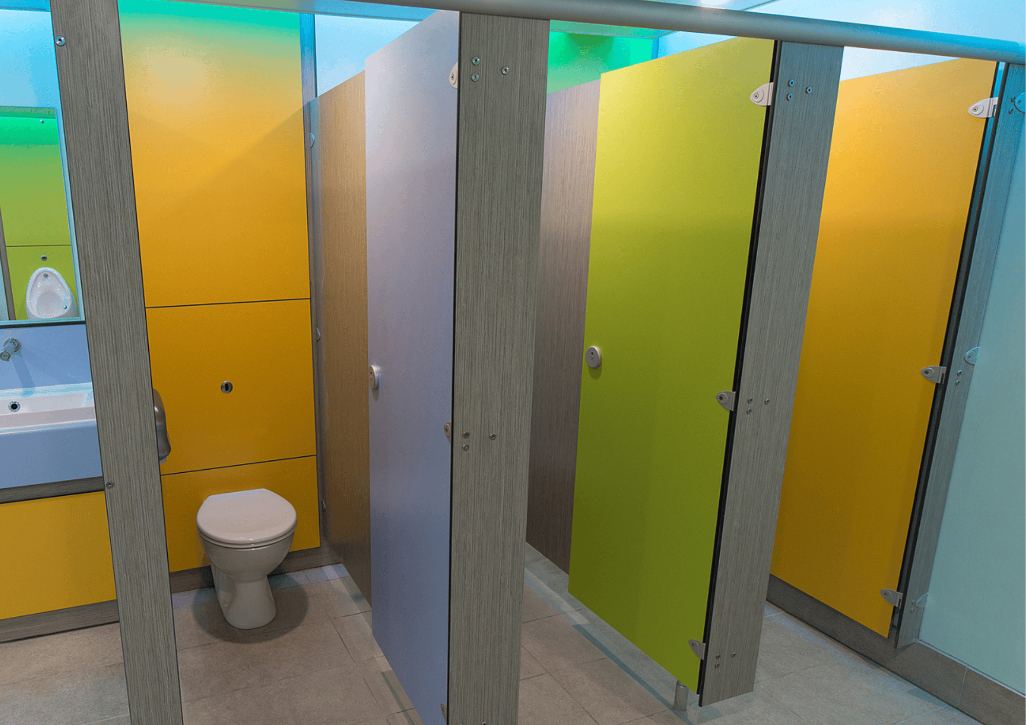 Brightly coloured toilet cubicles with grey partitions in a contemporary washroom.