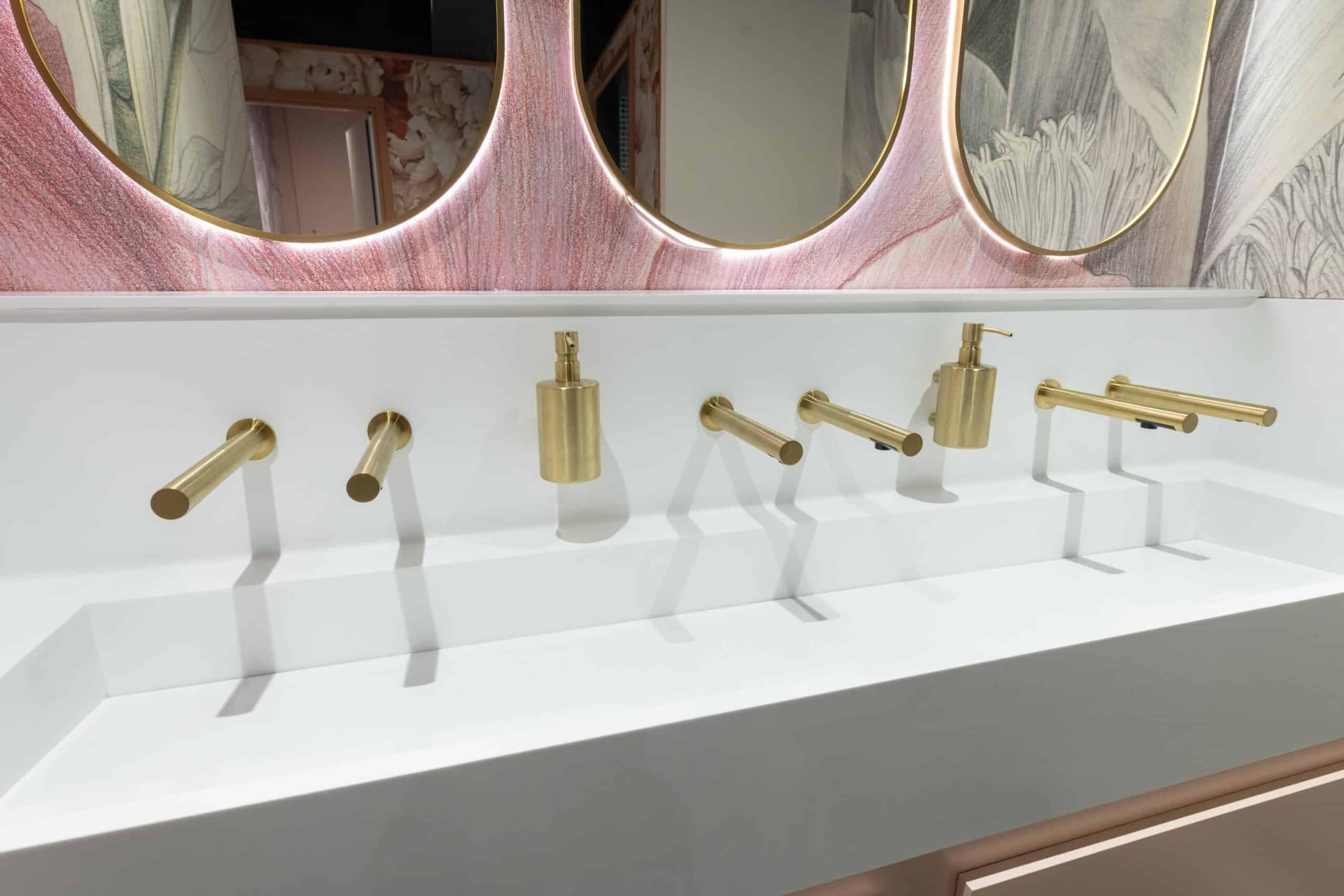 Modern washroom sink with gold taps and mirrors in a stylish setting.