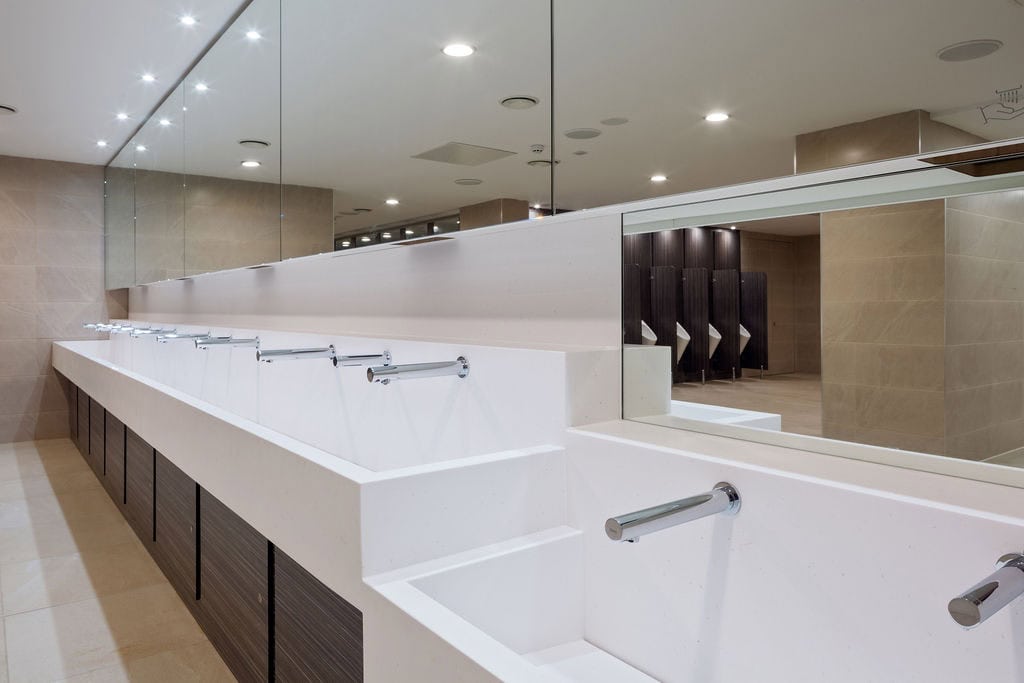 Solid Surface Wash Trough in a transport washroom with stainless steel wall-mounted taps and woodgrain underpanels
